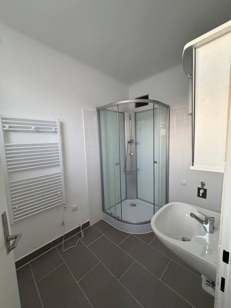 Modernes Badezimmer mit Duschkabine, Waschbecken und beheiztem Handtuchhalter.