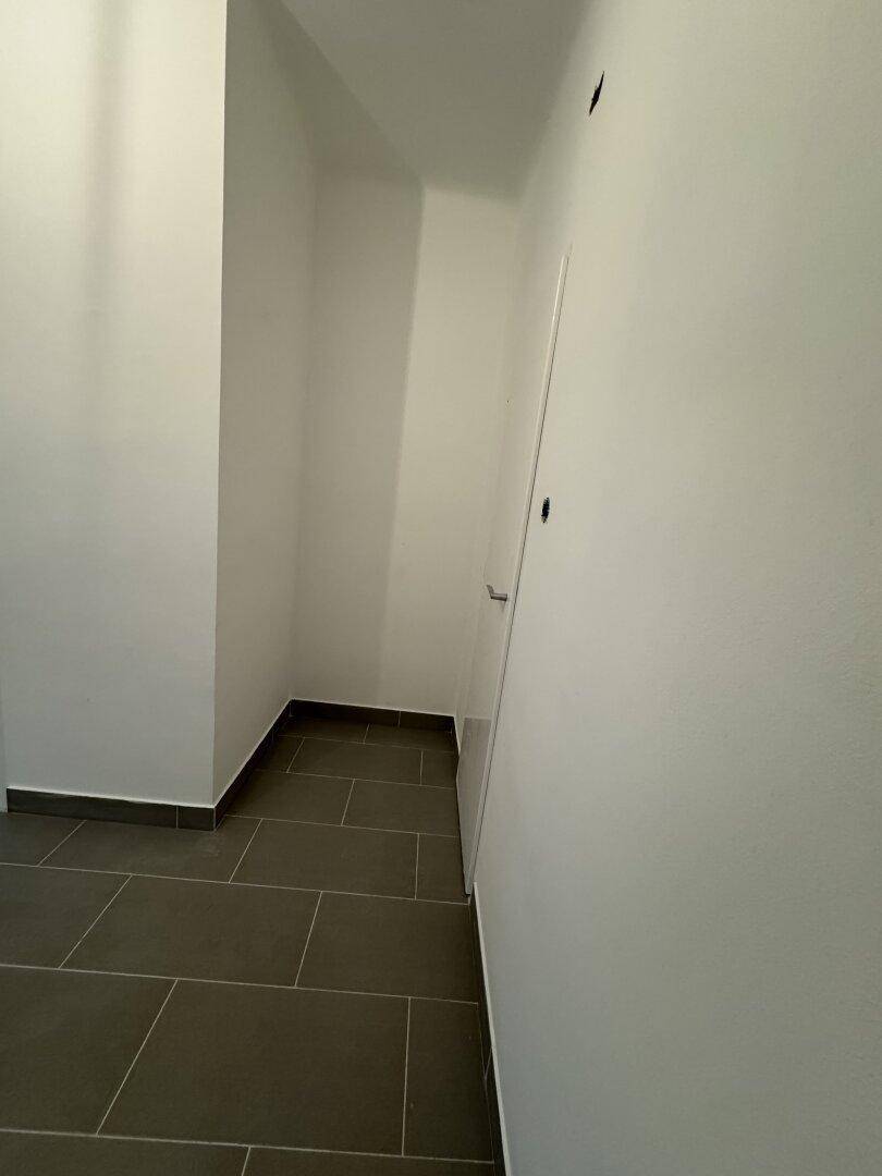 Heller Flur oder Abstellraum mit grauen Fliesen und weißen Wänden.