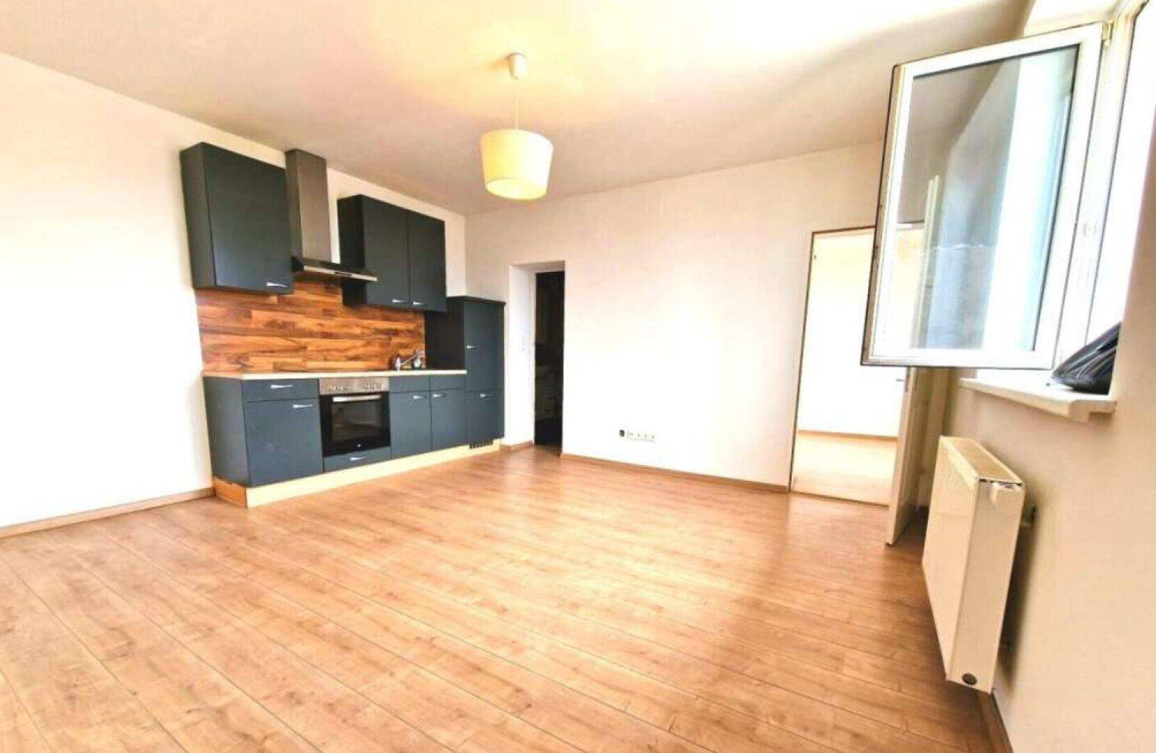 Offener Wohnbereich mit integrierter Küche, Laminatboden und einem Fenster mit Blick nach draußen.