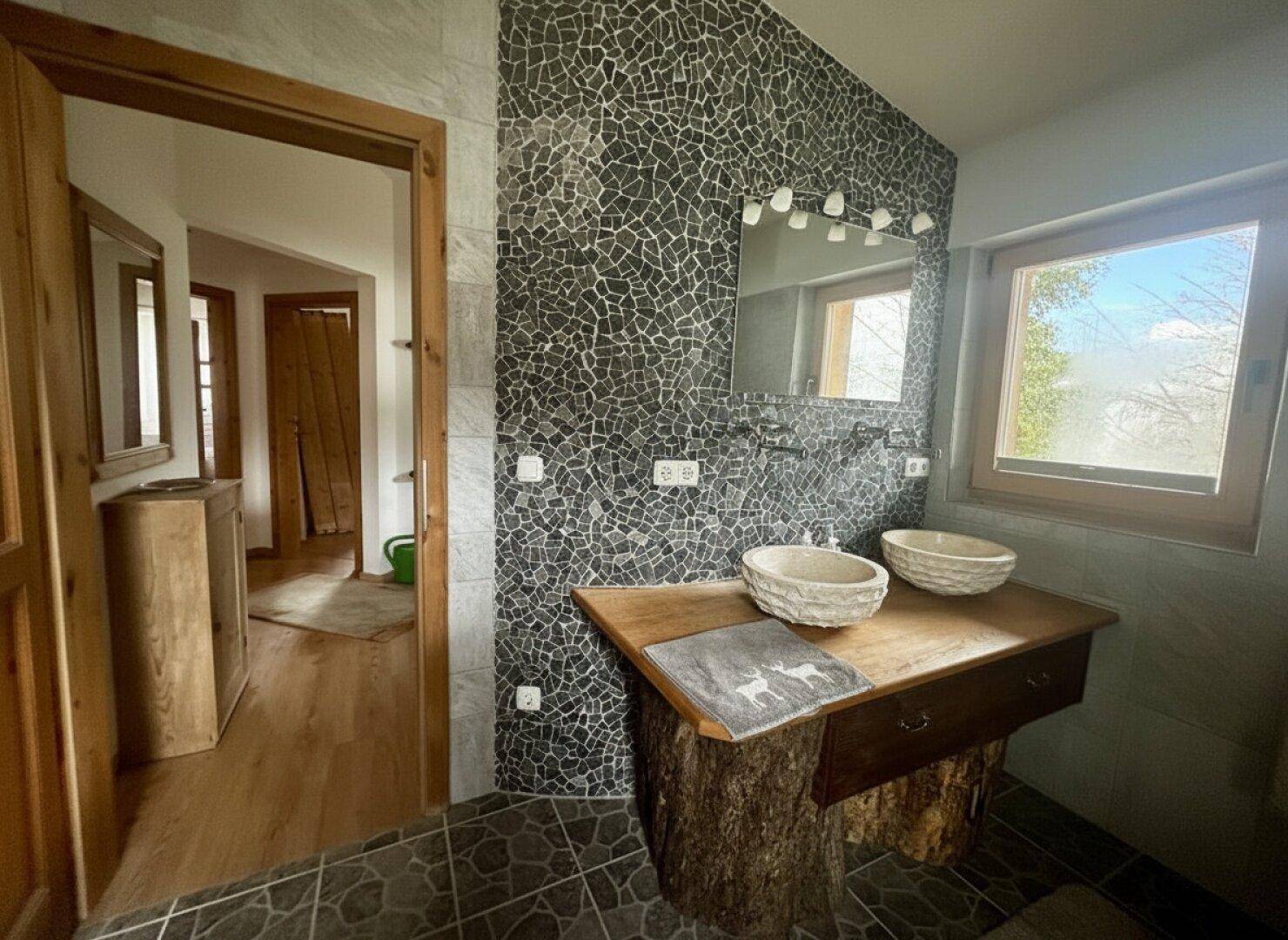 Stilvolles Badezimmer mit Doppelwaschbecken auf Holzplatte und Mosaikfliesenwand.