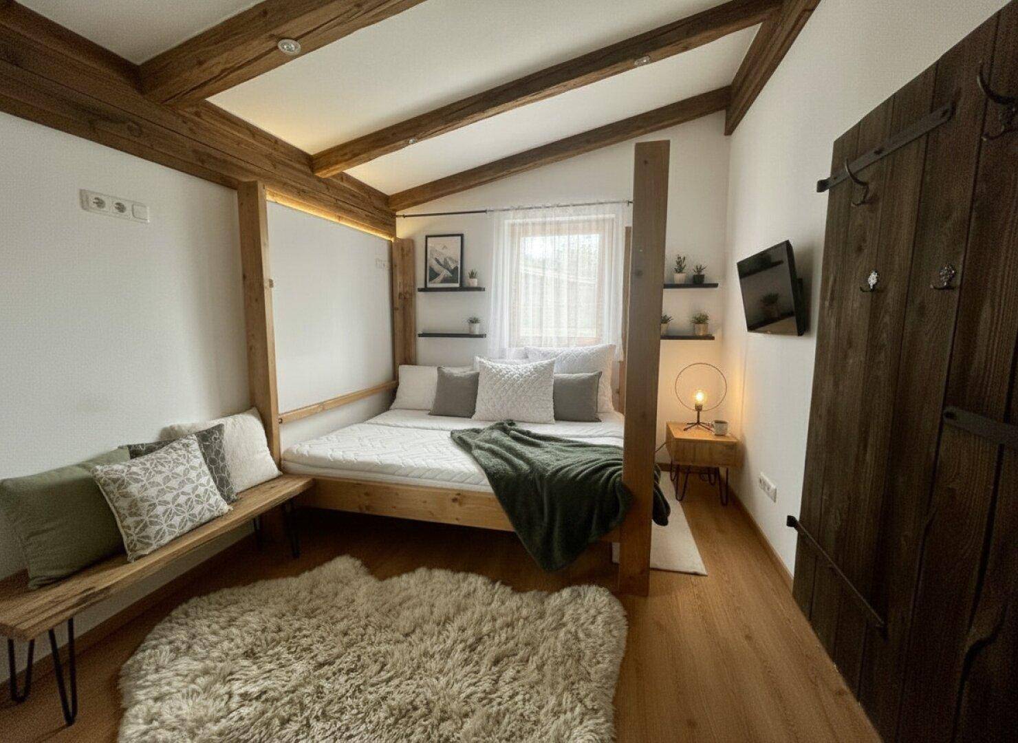 Gemütliches Schlafzimmer mit Holzbalken, modernem Bettgestell und rustikaler Holztür.