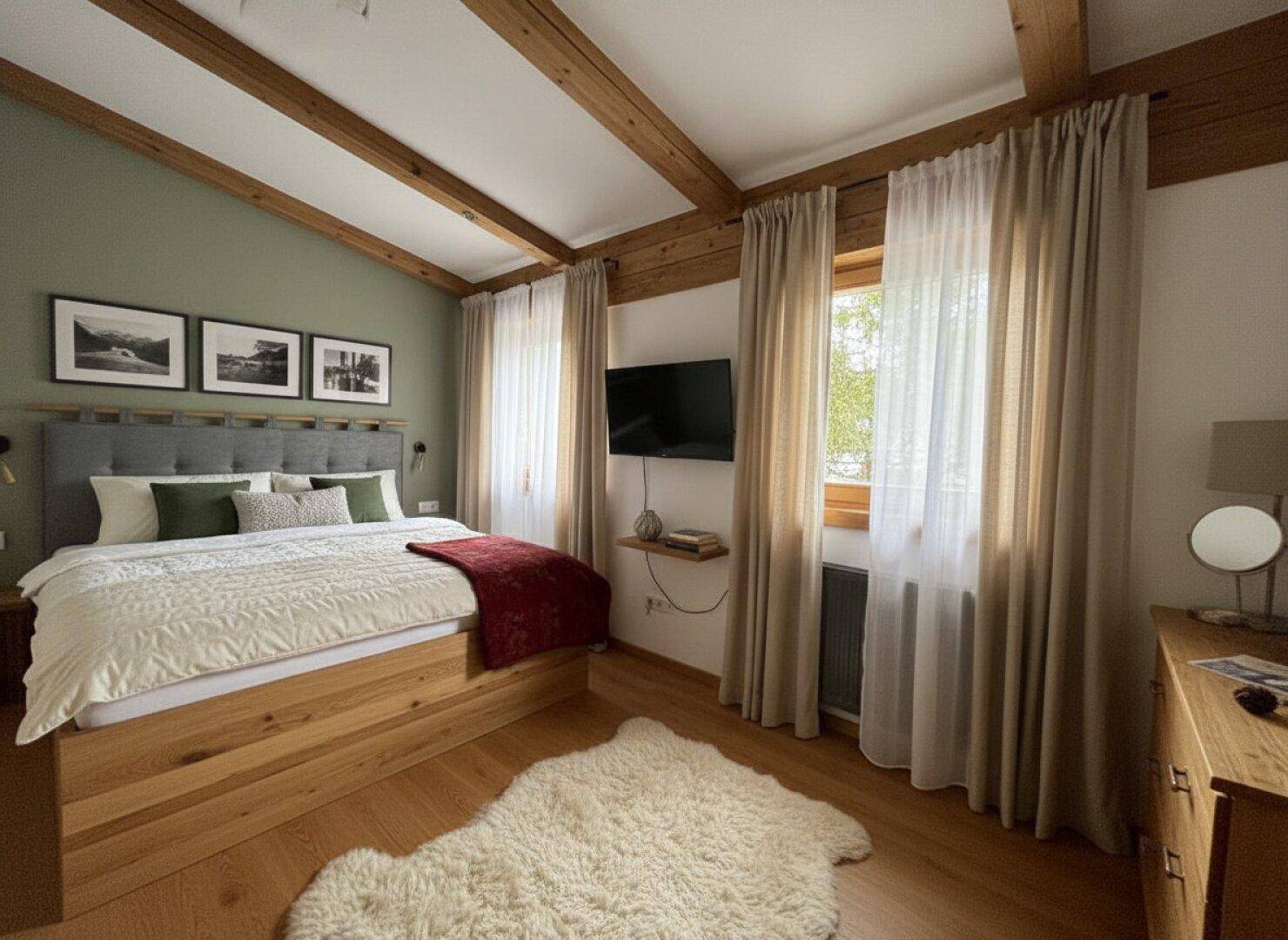 Helles Schlafzimmer mit Holzbalken, Doppelbett und grüner Akzentwand.