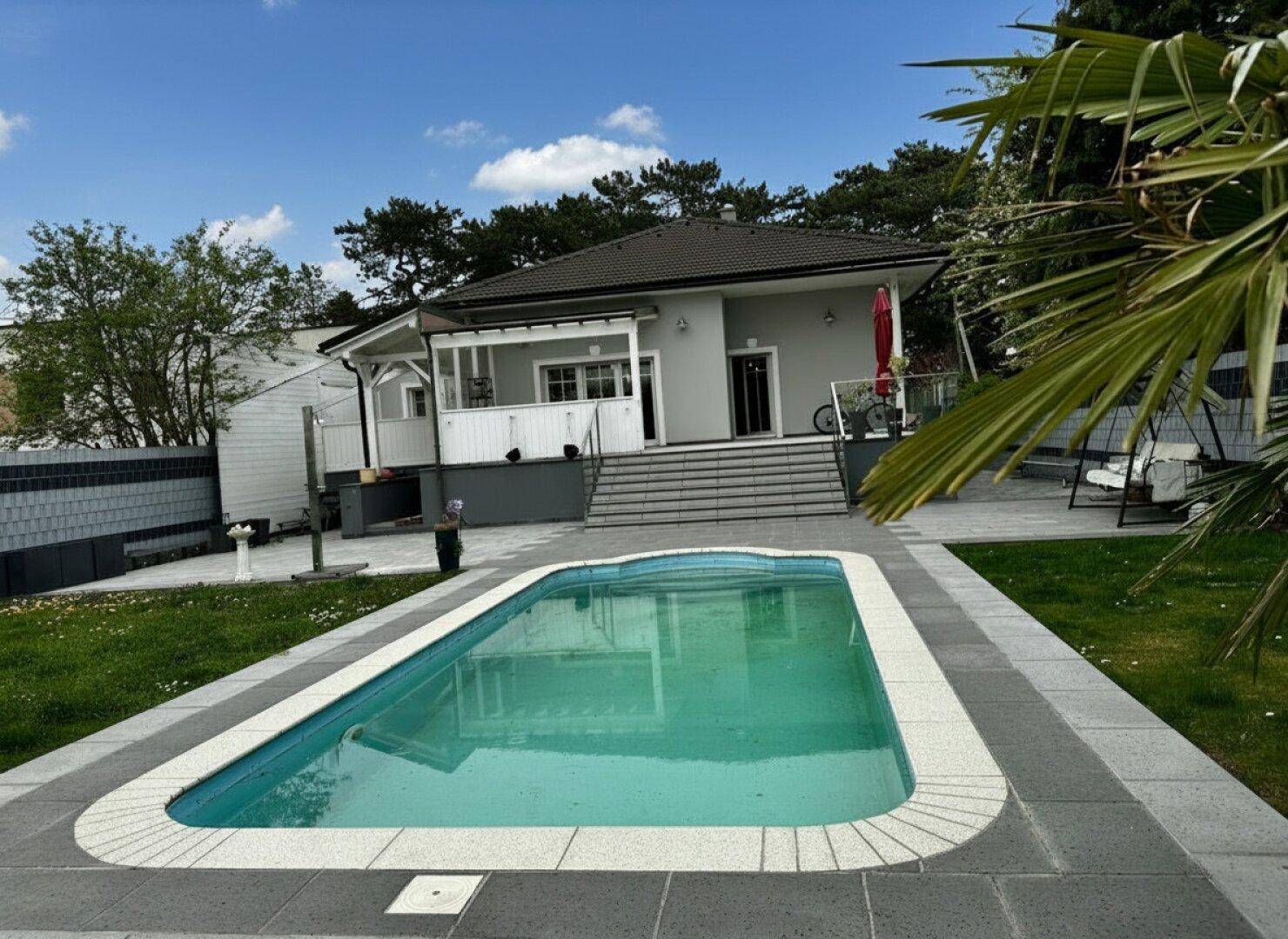 Rückansicht des Hauses mit großem Swimmingpool, Terrasse und gepflegtem Garten.