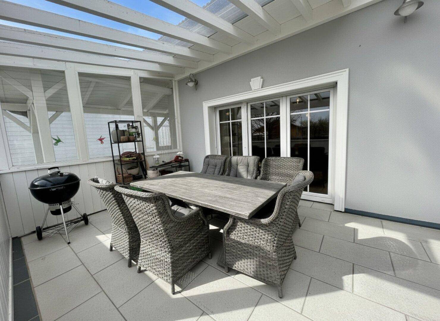 Überdachte Terrasse mit Esstisch und Stühlen, ideal für Mahlzeiten im Freien.