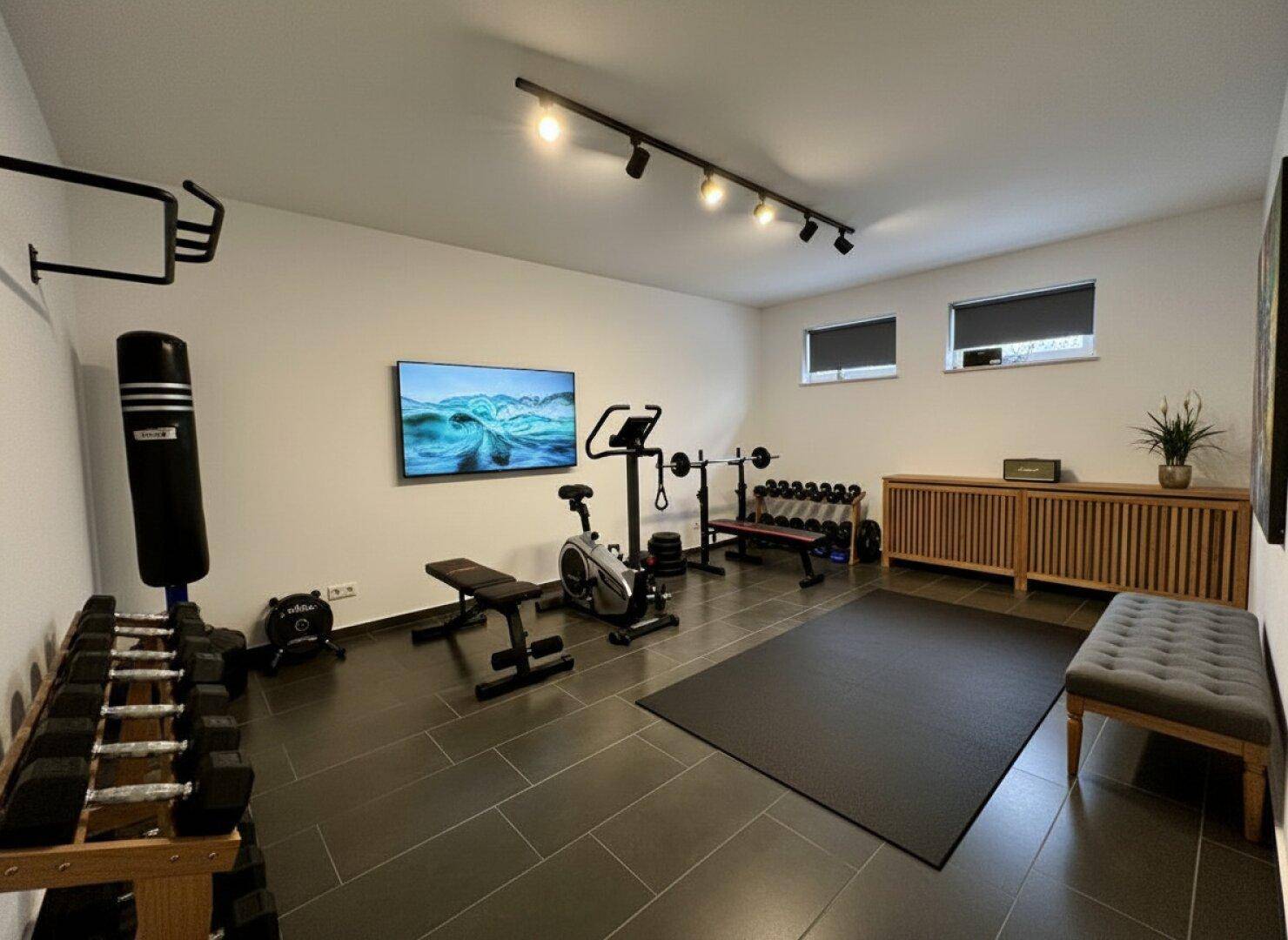 Gut ausgestatteter Fitnessraum mit verschiedenen Trainingsgeräten und Hanteln.