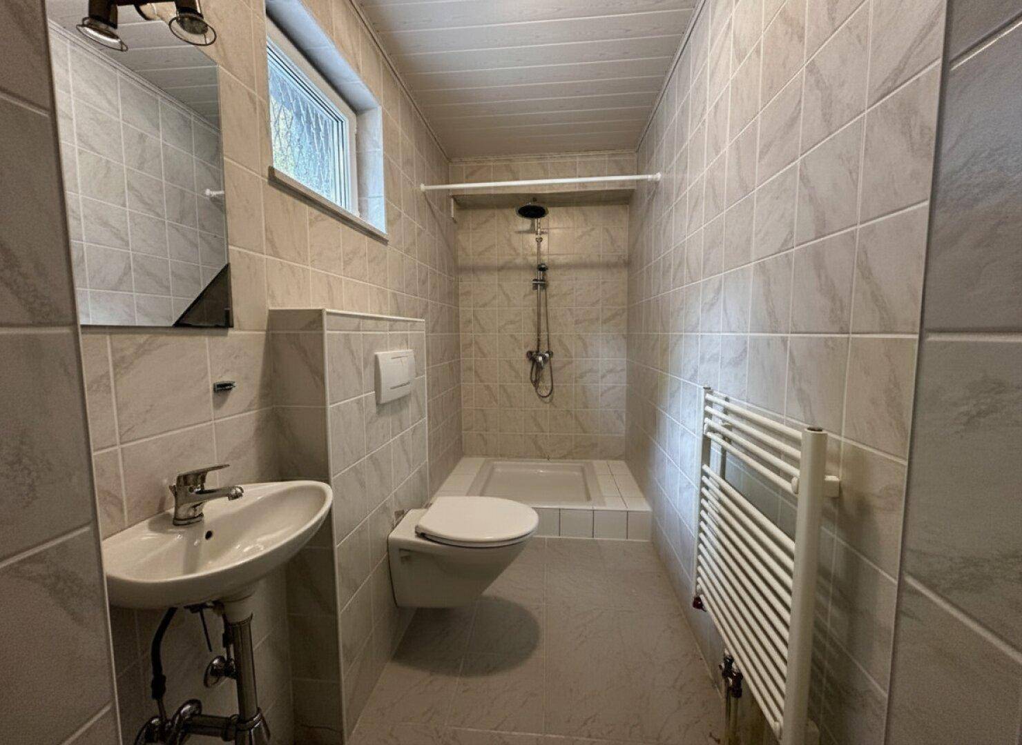 Modernes Badezimmer mit ebenerdiger Dusche, Wand-WC und Heizkörper.
