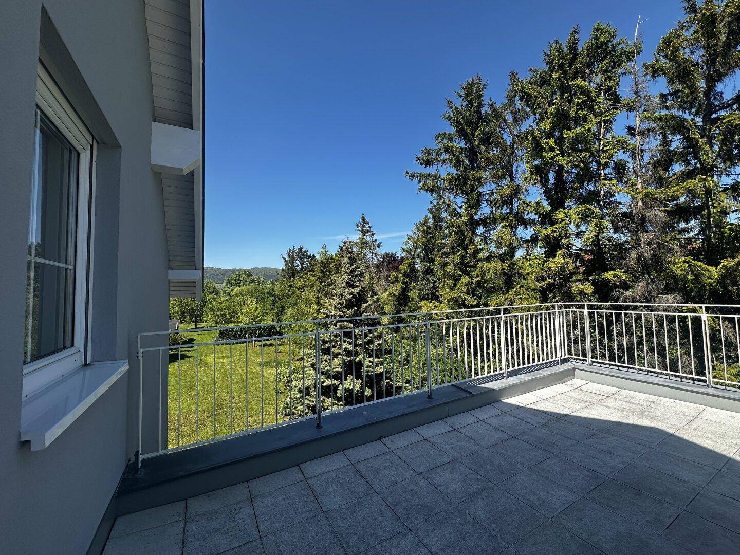Geräumige Dachterrasse mit Fliesenboden und weitem Blick ins Grüne und auf bewaldete Hügel.