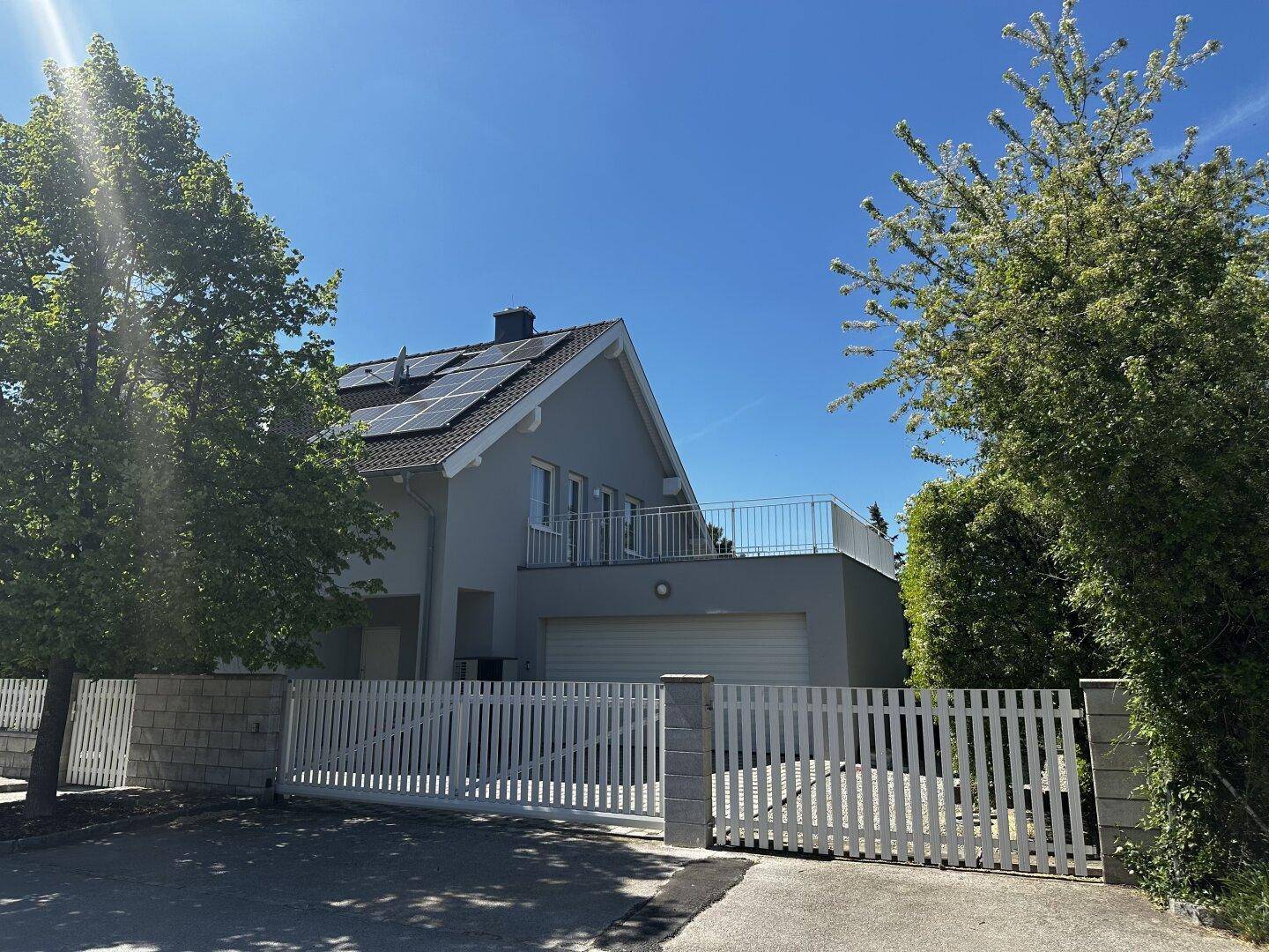 Ansicht des Hauses von der Straße mit weißem Zaun und Einfahrtstor.