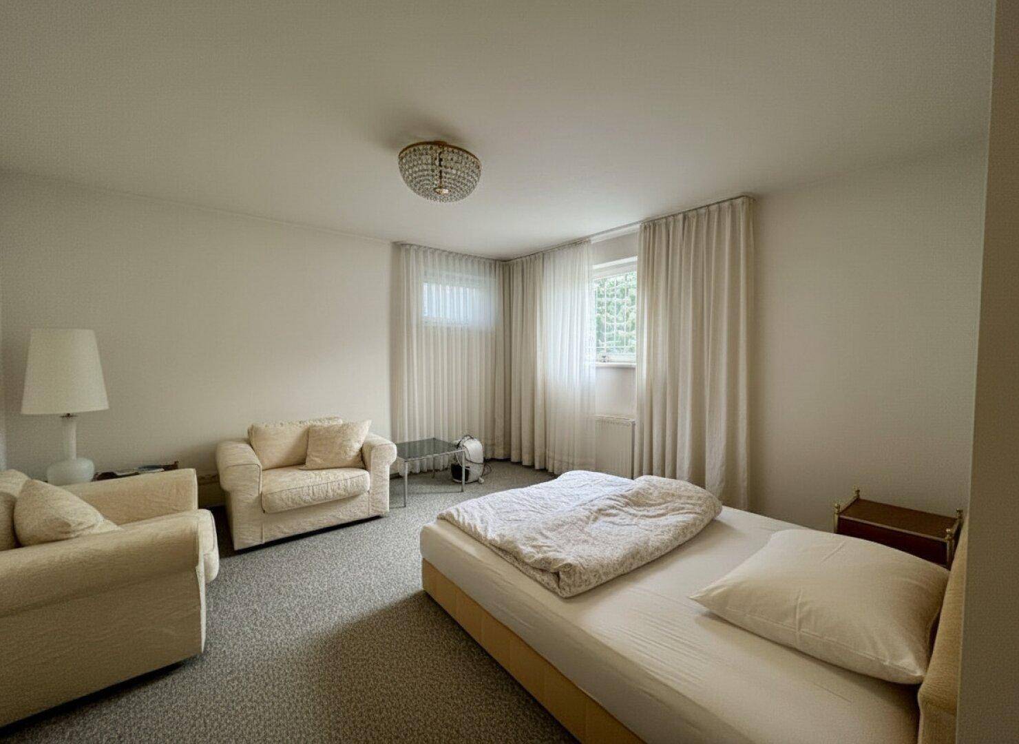 Gemütliches Schlafzimmer mit Teppichboden, Doppelbett und bequemen Sesseln am Fenster.