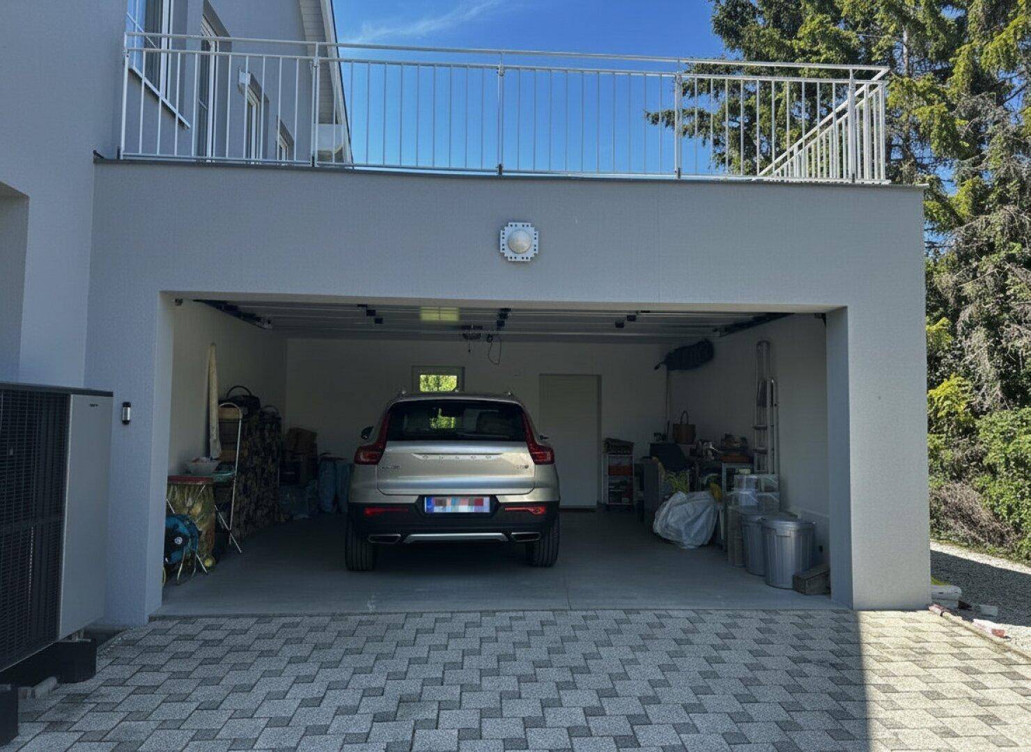 Offene Doppelgarage mit geparktem Auto und darüberliegender Dachterrasse mit Geländer.