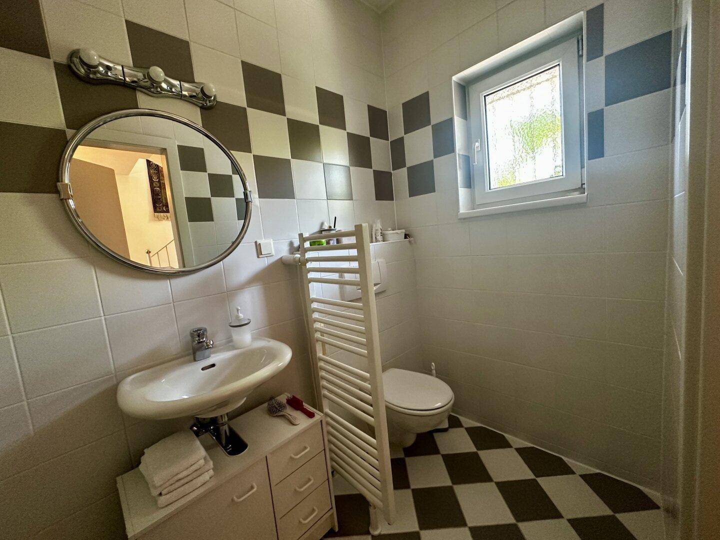Modernes Gäste-WC mit Schachbrettmuster-Fliesen, Fenster und beheiztem Handtuchhalter.