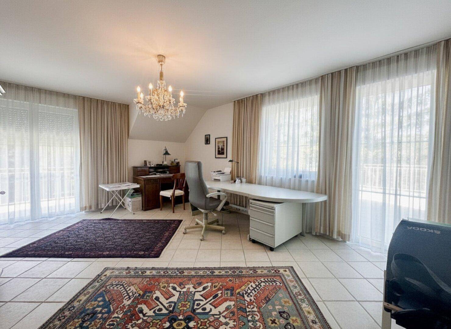 Großes Arbeitszimmer mit Fliesenboden, Kronleuchter und Zugang zu einem Balkon.