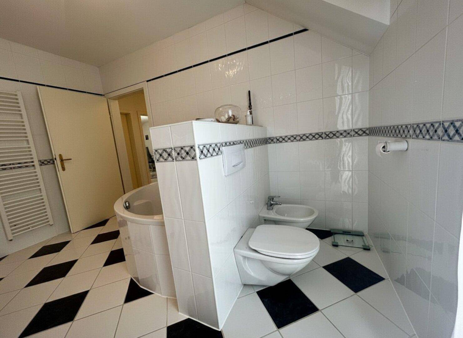 Badezimmer mit Badewanne, wandmontiertem WC, Bidet und Schachbrettmuster-Fliesen.