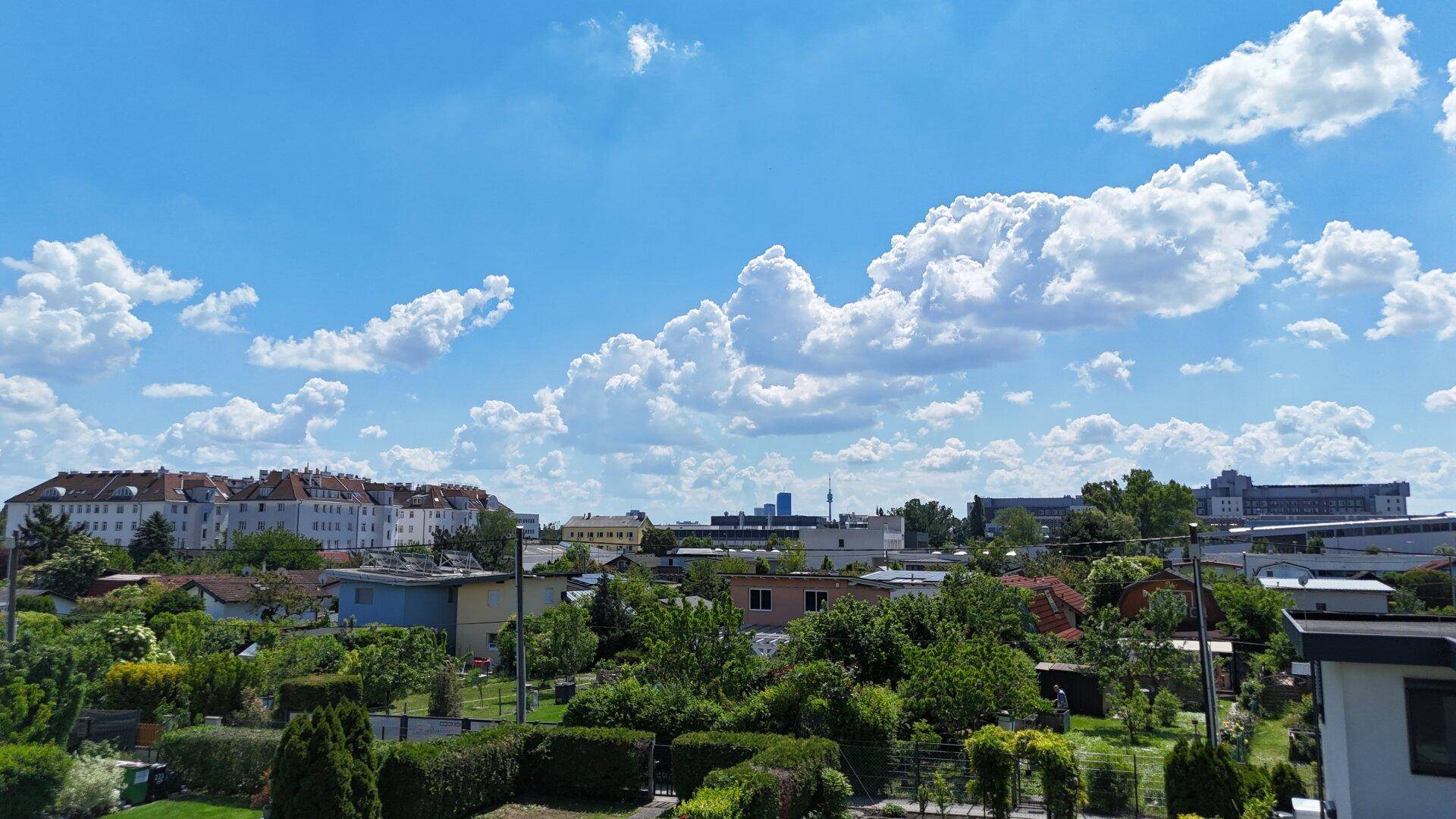 Weitläufiger Blick über eine grüne Wohnsiedlung mit Gärten und Gebäuden unter blauem Himmel.
