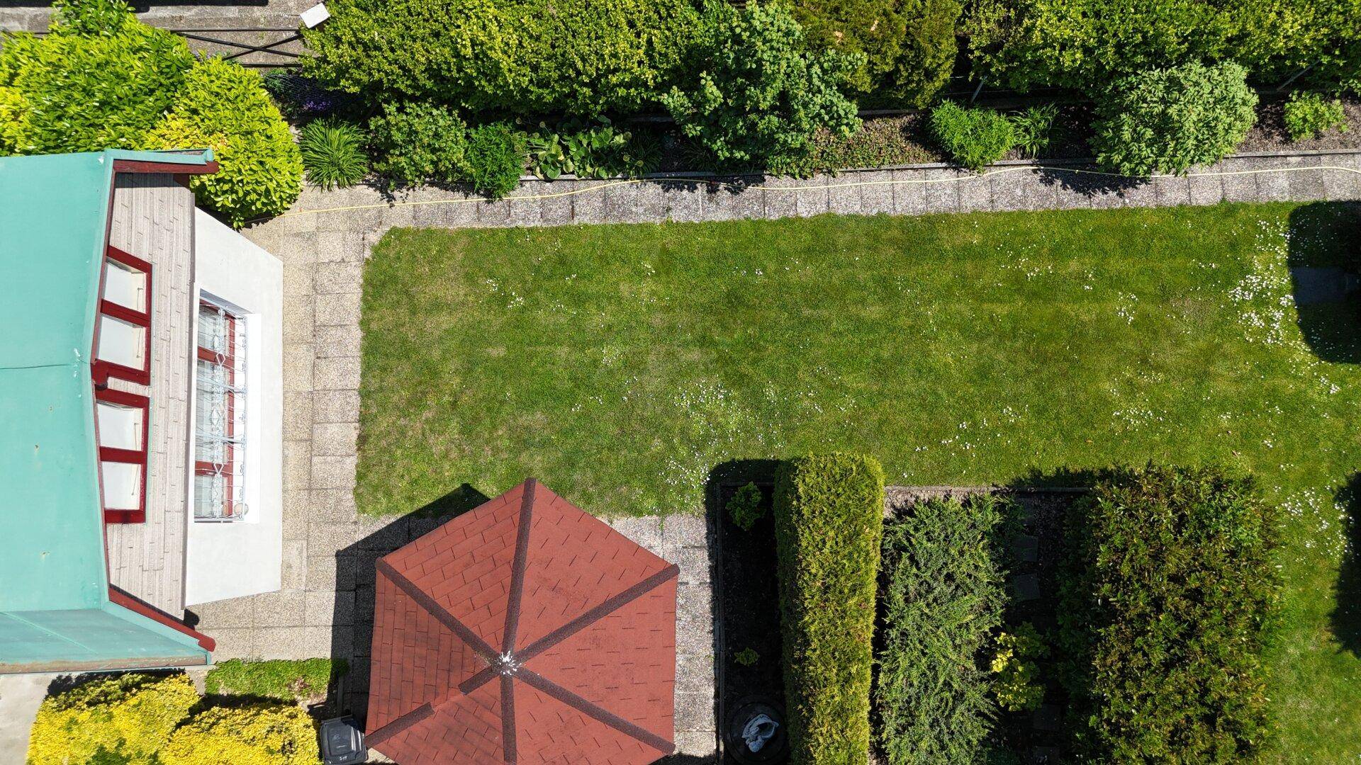 Luftaufnahme eines Teils des Hauses mit Garten, Rasenfläche, Hecken und einem roten Pavillon.