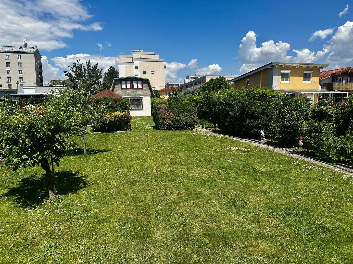 Weitläufiger Gartenbereich mit Rasen, Bäumen und Blick auf umliegende Wohngebäude.
