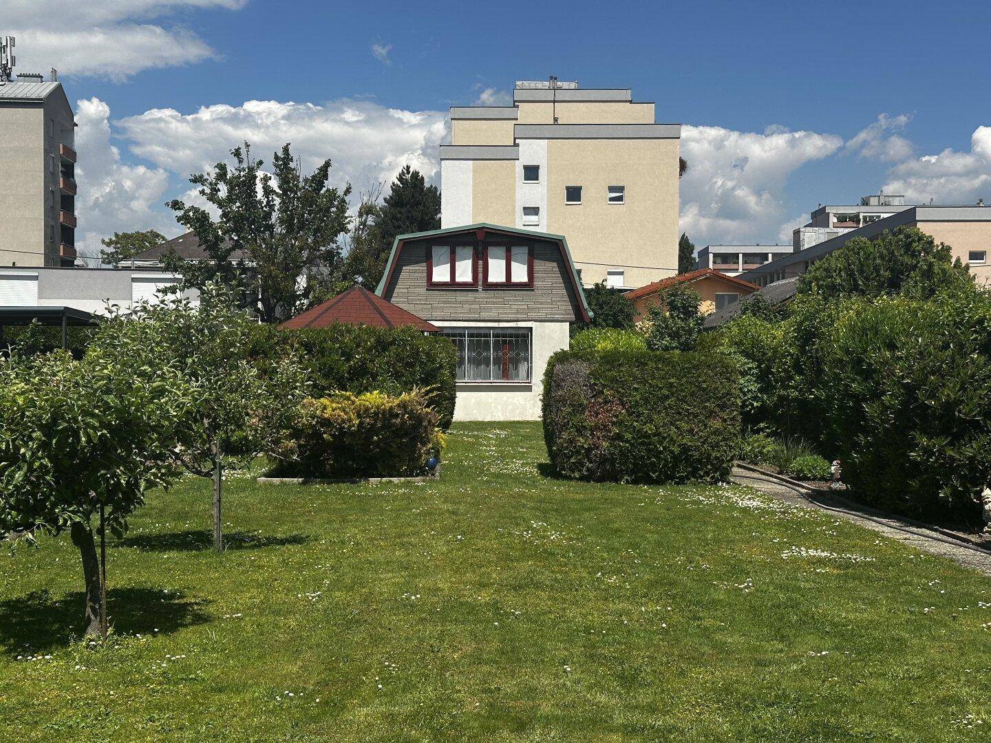 Ansicht des Hauses mit Mansarddach und Pavillon, umgeben von einem gepflegten Garten.