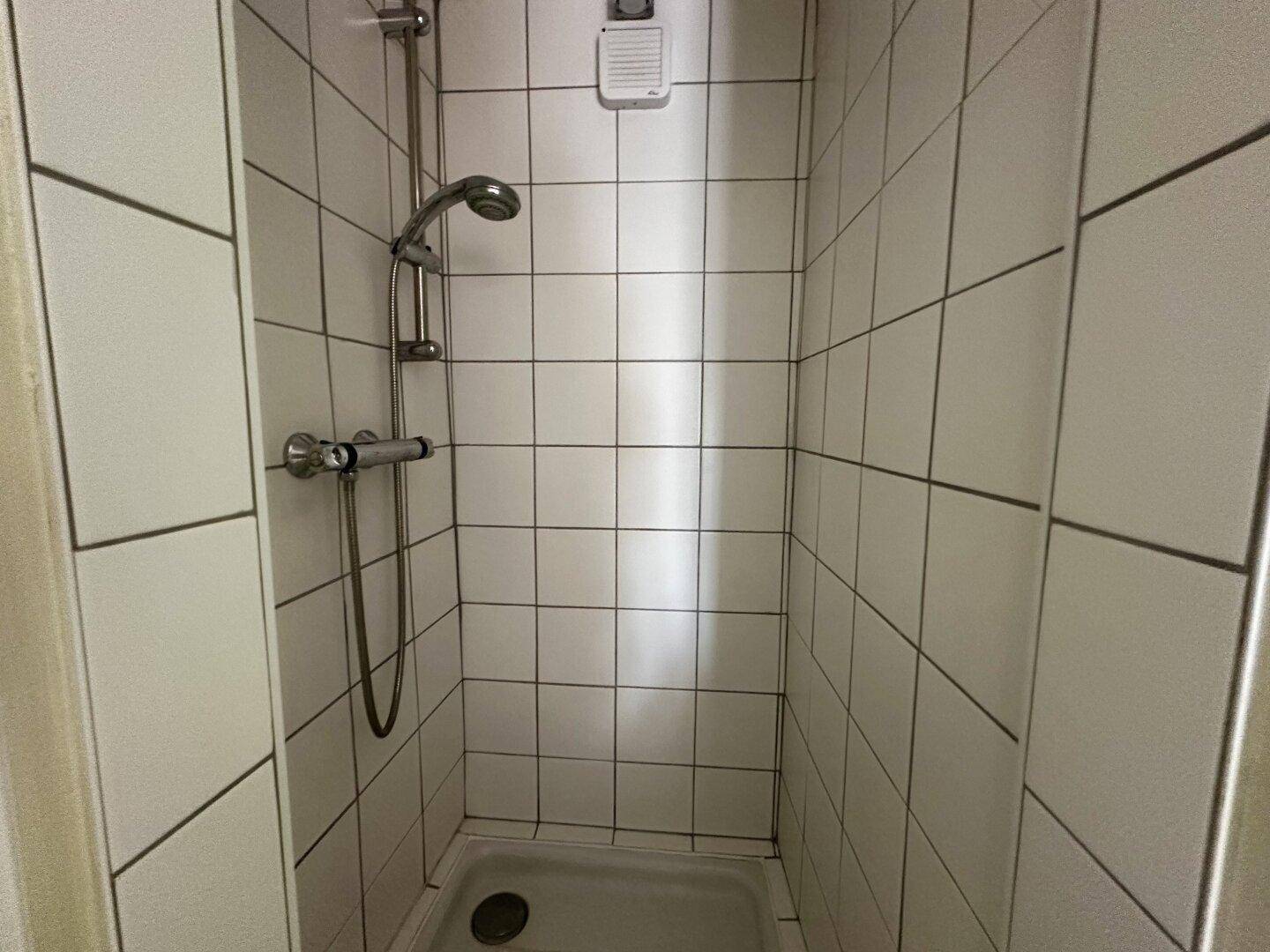 Einfache Duschkabine mit weißen Fliesen und Duscharmatur.