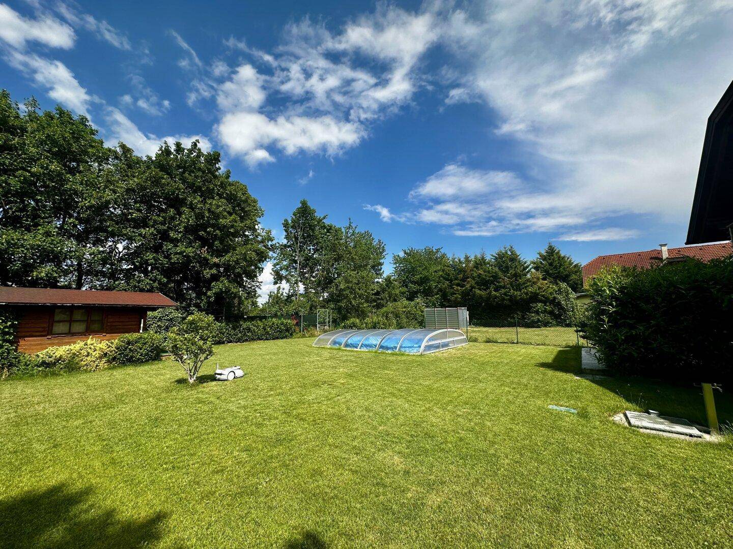 Weitläufiger Gartenbereich mit Schwimmbecken, umgeben von Bäumen und viel Grünfläche.