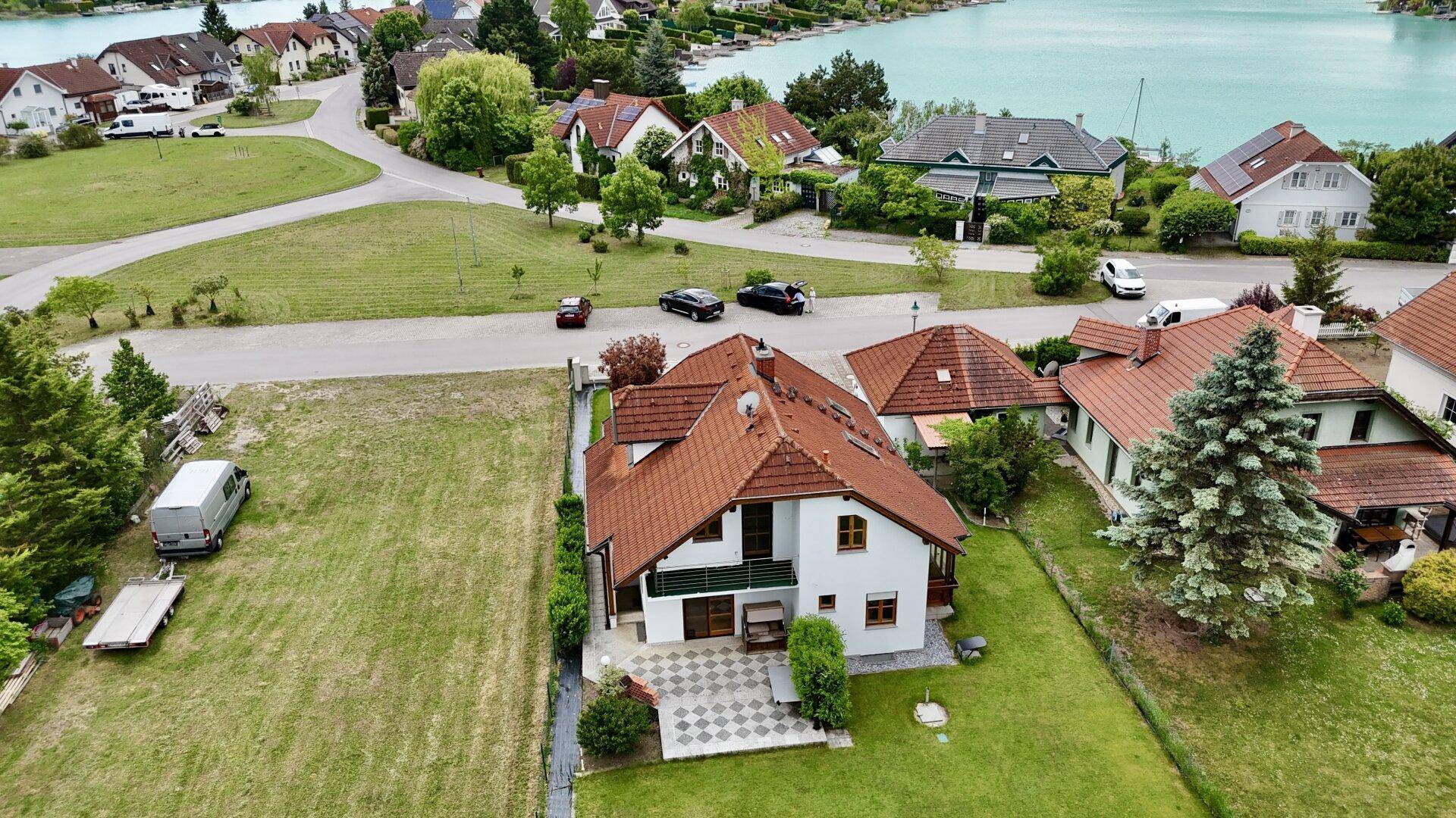 Luftaufnahme des Hauses mit Garten, Terrasse und der umliegenden Wohnsiedlung am Seeufer.