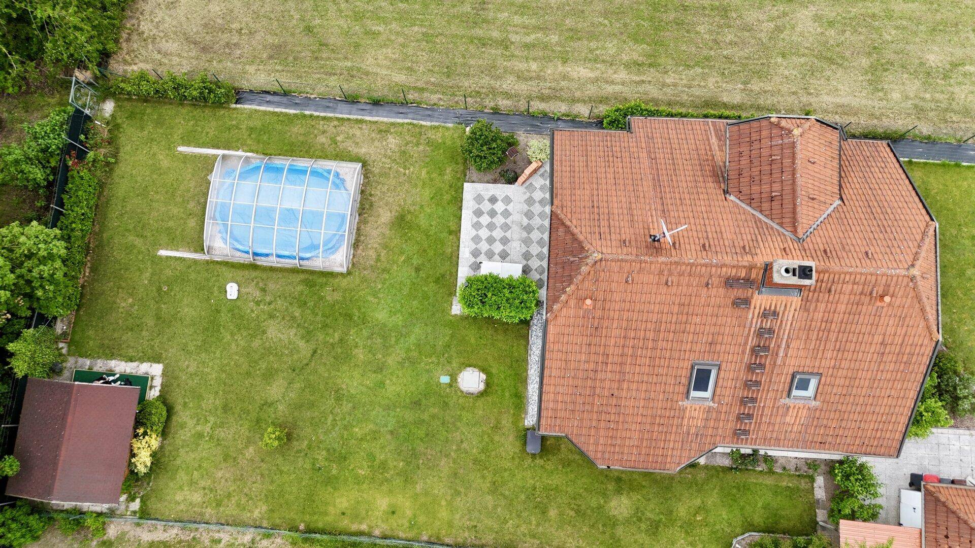 Draufsicht auf das Haus mit rotem Ziegeldach, Garten, Pool und gepflasterter Terrasse.