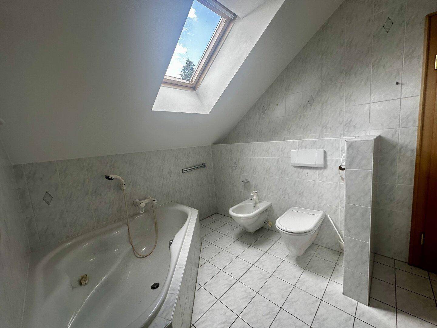 Badezimmer im Dachgeschoss mit Badewanne, Bidet, WC, Fliesen und Dachfenster.