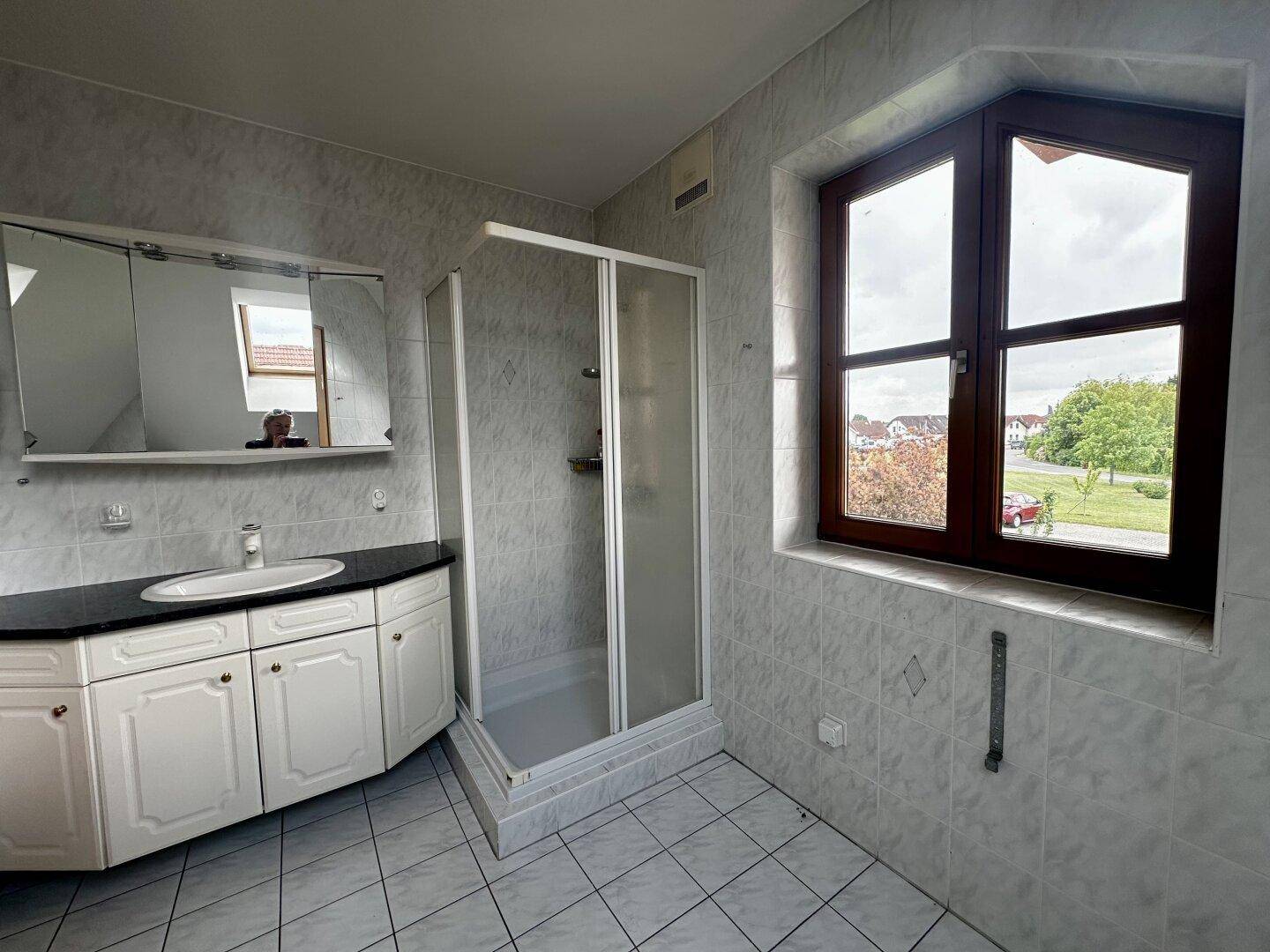 Badezimmer mit Duschkabine, Waschtisch, Spiegelschrank und Fenster.