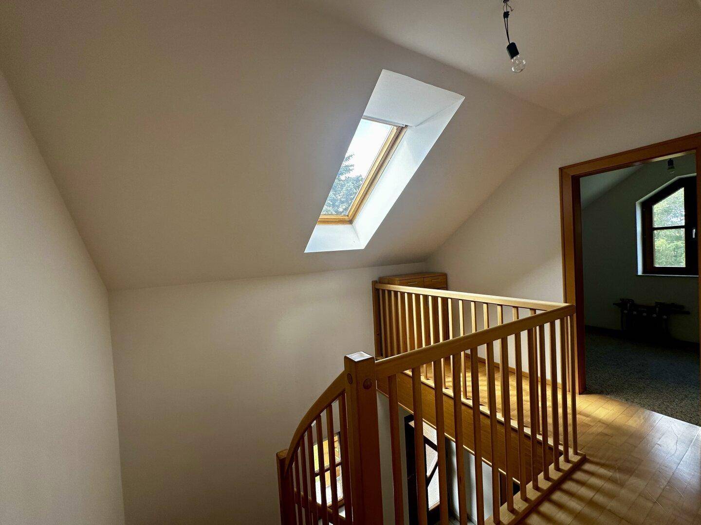 Heller Treppenaufgang im Dachgeschoss mit Holzgeländer und Dachfenster.