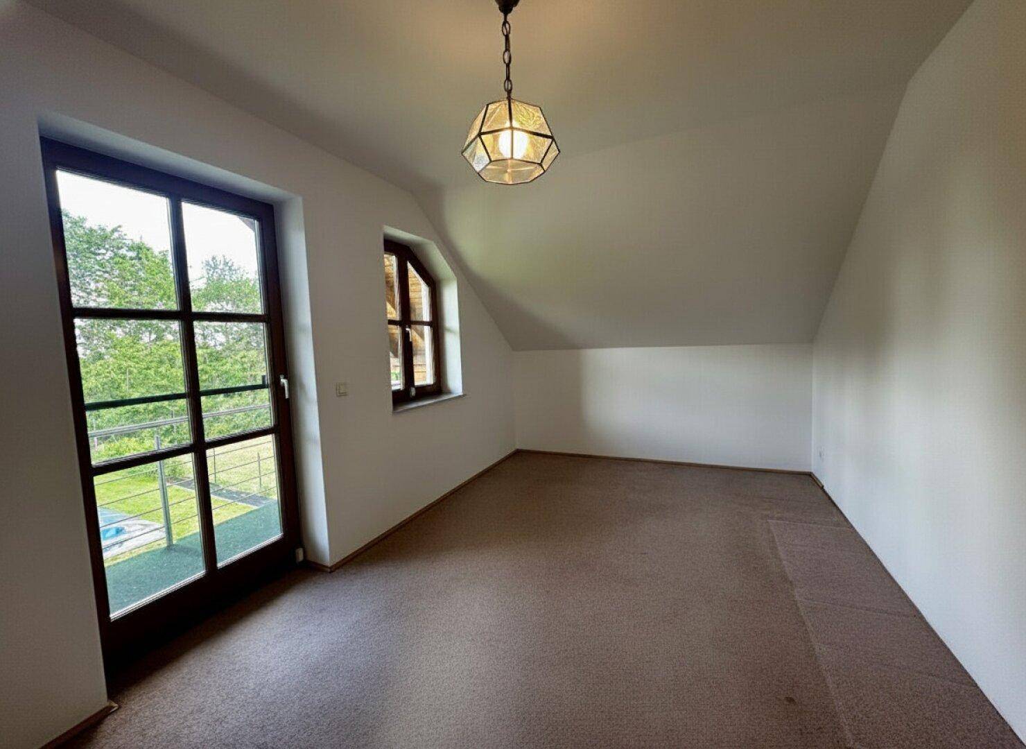 Dachgeschosszimmer mit Teppichboden, Balkonzugang und schräger Decke.