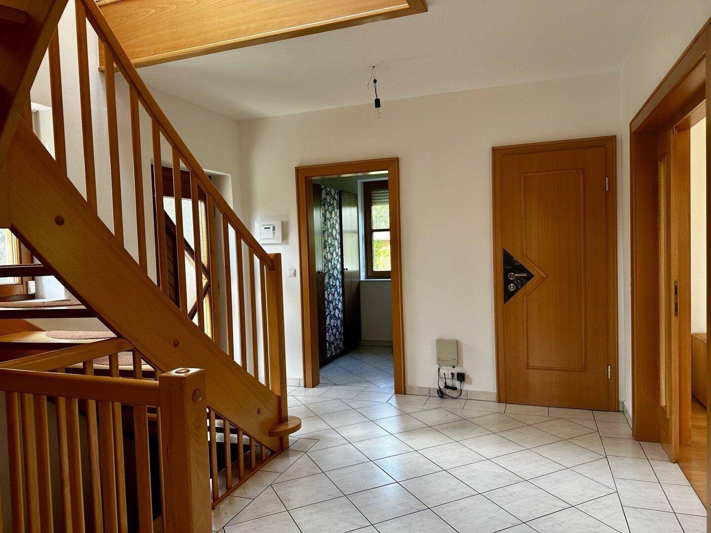 Geräumiger Flur mit Holztreppe, Fliesenboden und Zugang zu weiteren Räumen.