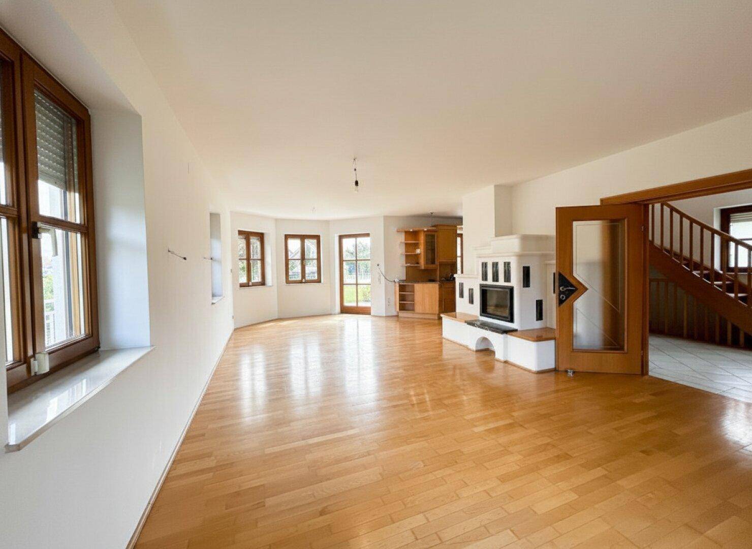 Großzügiges Wohnzimmer mit Parkettboden, Kachelofen und Zugang zur Küche.