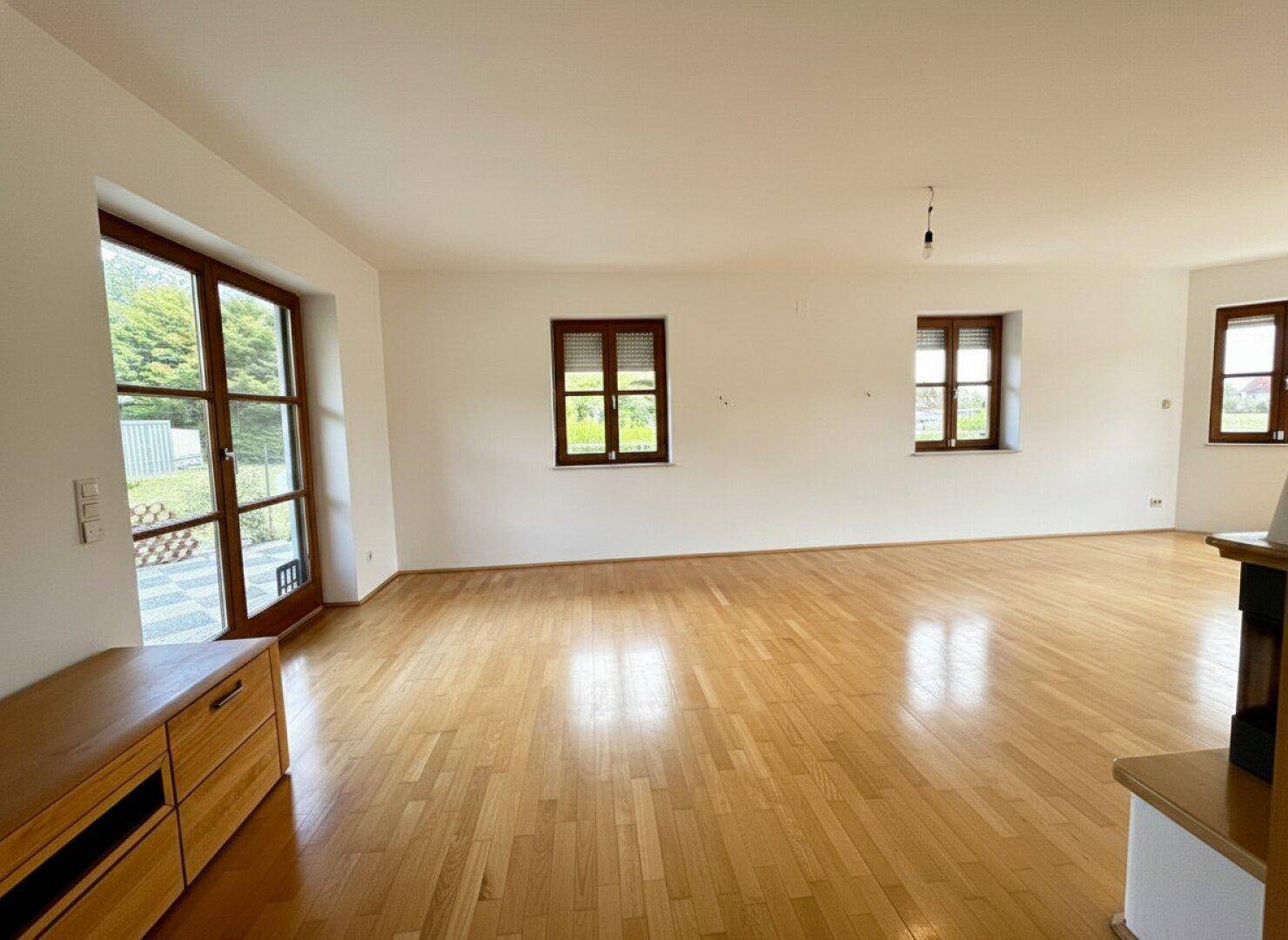 Geräumiges Wohnzimmer mit Parkettboden, hellen Wänden und Zugang zur Terrasse.