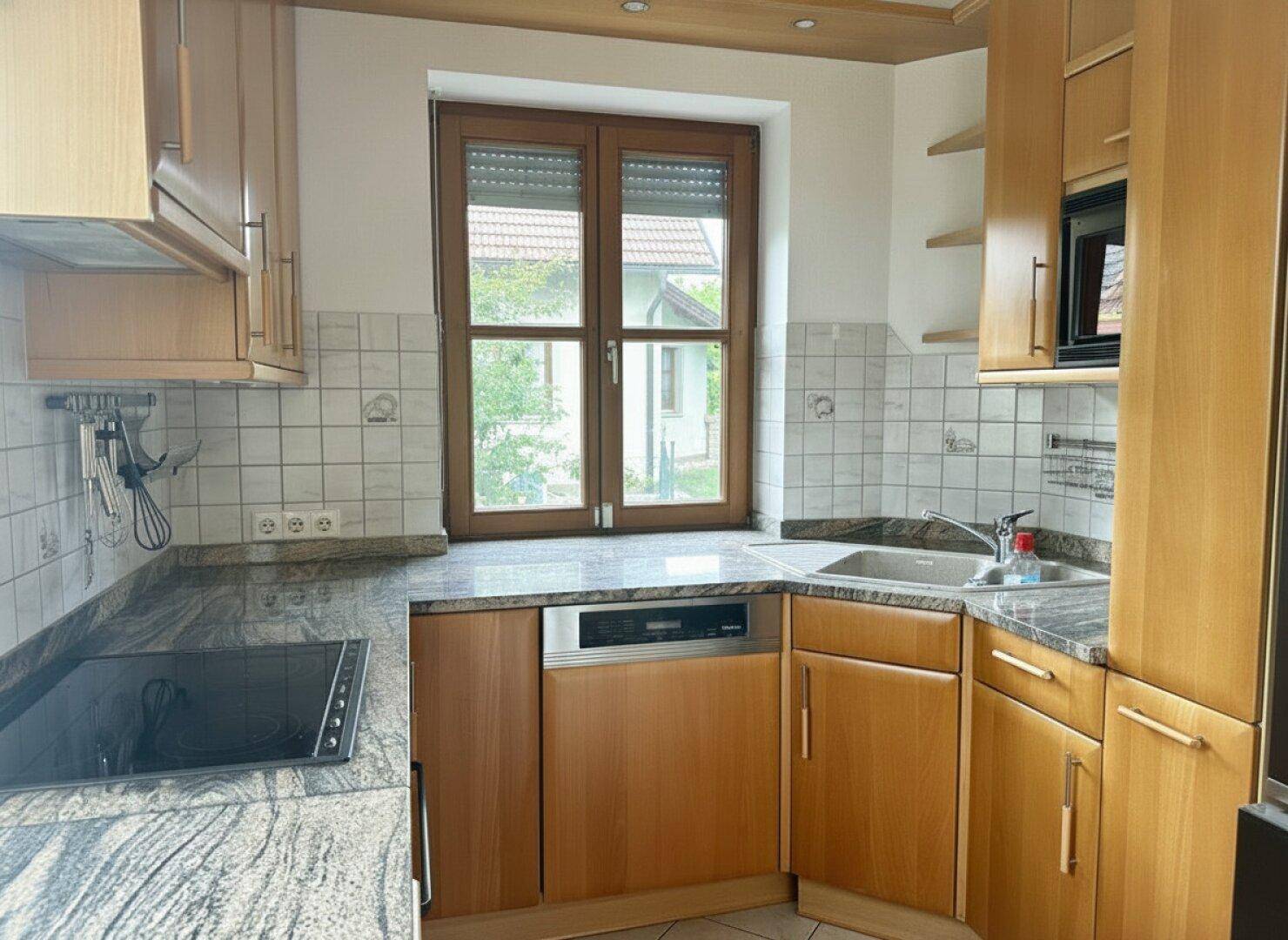 Funktionale Küche mit Holzschränken, Granitarbeitsplatte, Induktionskochfeld und Fenster.