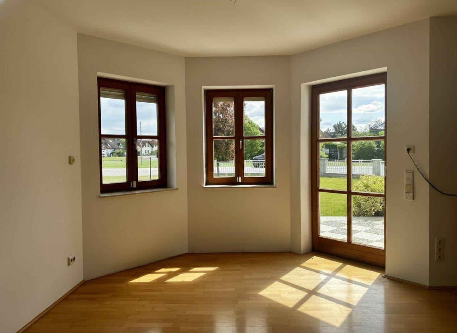 Heller Wohnbereich mit Parkettboden, großen Fenstern und Terrassenzugang.