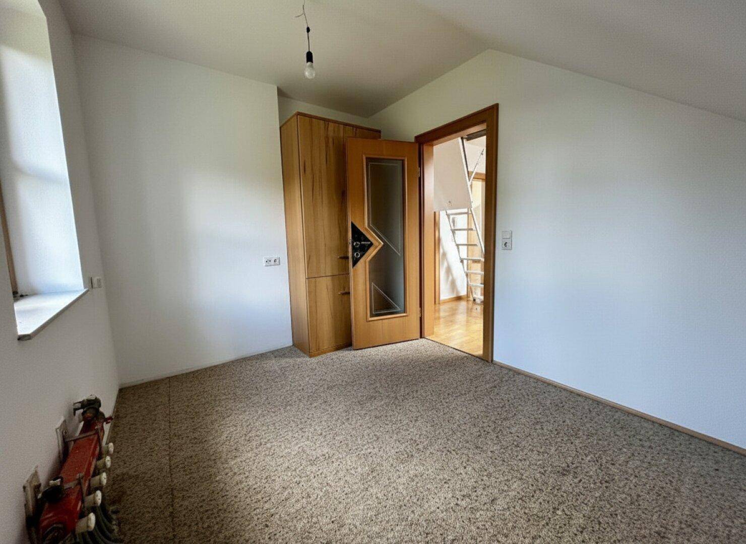 Dachgeschosszimmer mit Teppichboden, Kleiderschrank und Zugang zu weiteren Räumen.