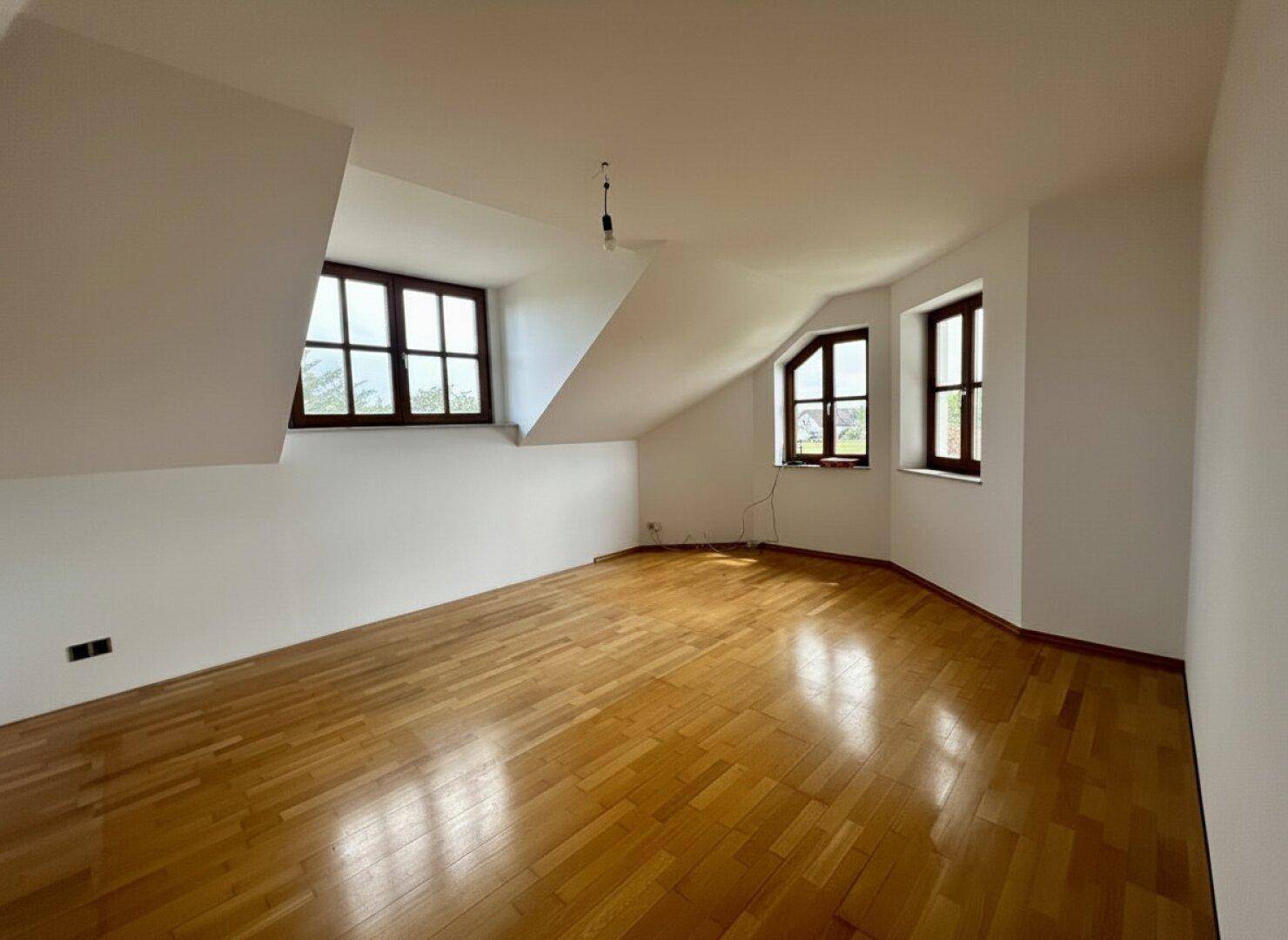 Helles Schlafzimmer im Dachgeschoss mit Parkettboden, Schrägen und mehreren Fenstern.