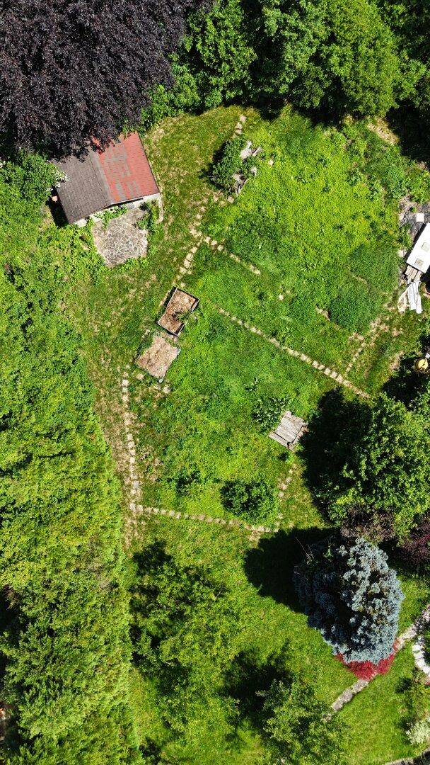 Luftaufnahme eines großen, grünen Gartengrundstücks mit Schuppen und Wegen, umgeben von Bäumen.