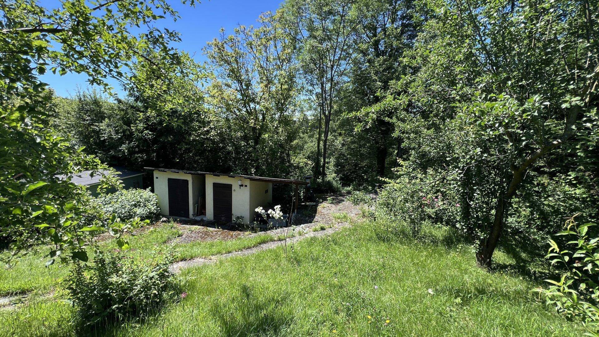 Einfaches Nebengebäude mit zwei Türen in einer grünen Gartenlandschaft, umgeben von Bäumen.