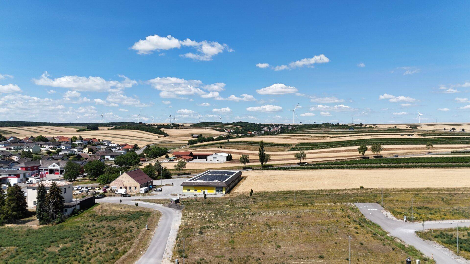 Weitläufige Luftaufnahme der ländlichen Umgebung mit Feldern, Windrädern und einem Dorf.