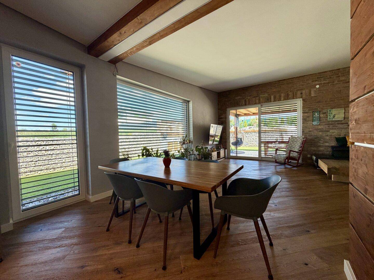 Essbereich mit Holztisch, modernen Stühlen und großen Fenstern mit Blick ins Grüne.