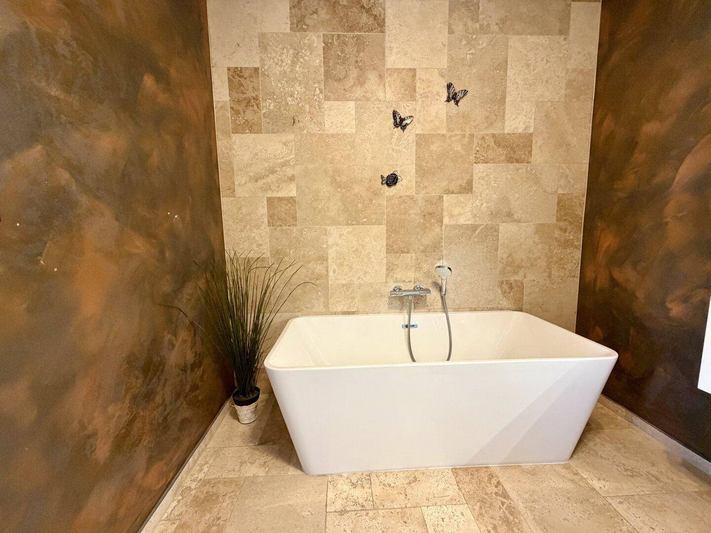 Elegante freistehende Badewanne in einem gefliesten Badezimmer mit dekorativer Wandgestaltung.