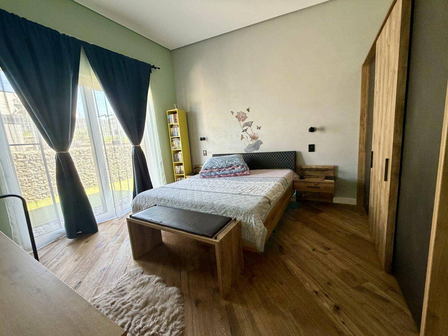 Schlafzimmer mit Holzboden, Doppelbett und großer Glastür, die viel Licht hereinlässt.