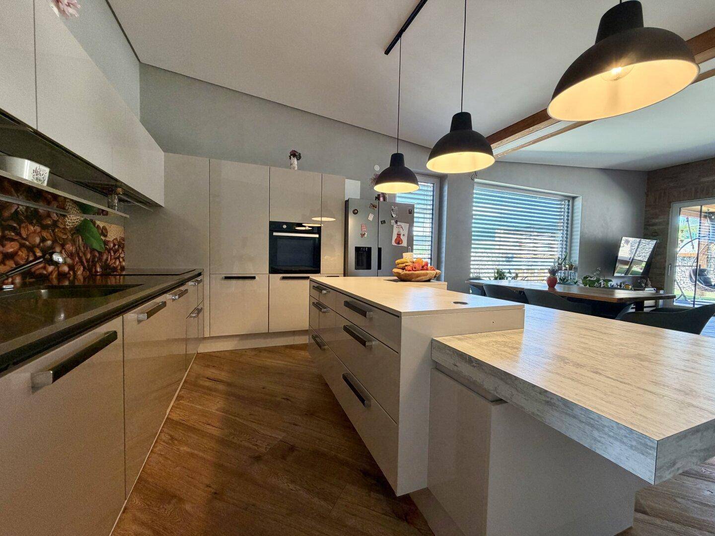 Moderne Einbauküche mit Kücheninsel, dunklen Hängelampen und Holzboden.