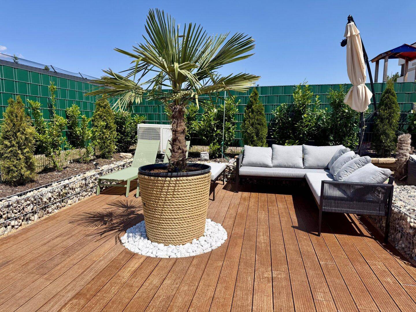 Gemütlicher Sitzbereich auf einer Holzterrasse mit Lounge-Möbeln und einer großen Palme.