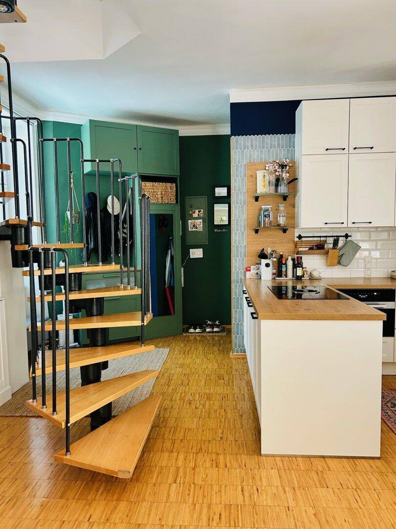Moderne offene Küche mit Kochinsel und Holztheke, daneben eine stilvolle Wendeltreppe und grüne Wand.