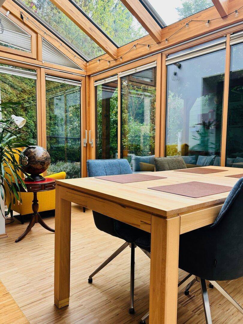 Heller Wintergarten mit Holzbalken, Esstisch und Blick in den Garten, ideal für gesellige Stunden.