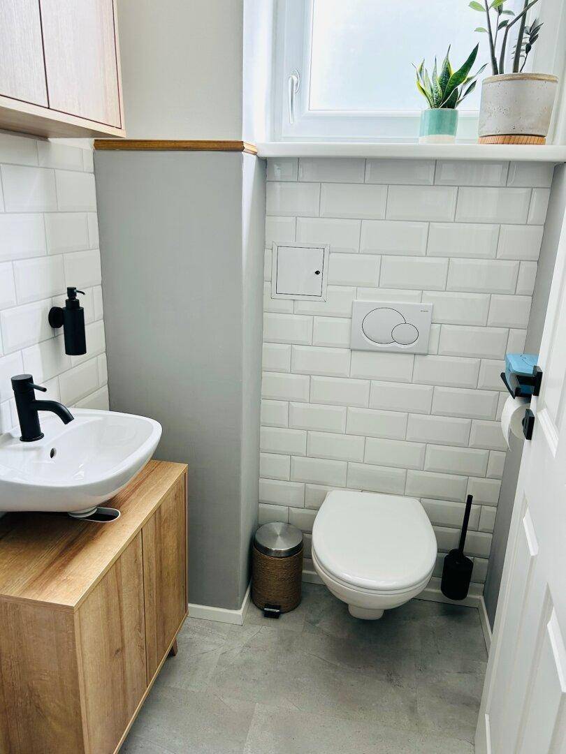 Modernes Gäste-WC mit weißer U-Bahn-Fliesenwand, kleinem Waschbecken und Fenster für Tageslicht.