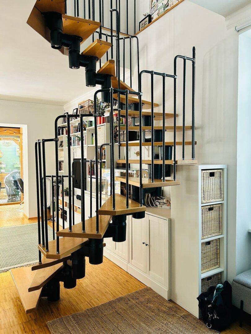 Elegante Wendeltreppe mit Holzstufen und schwarzem Geländer, daneben praktische Einbauschränke.