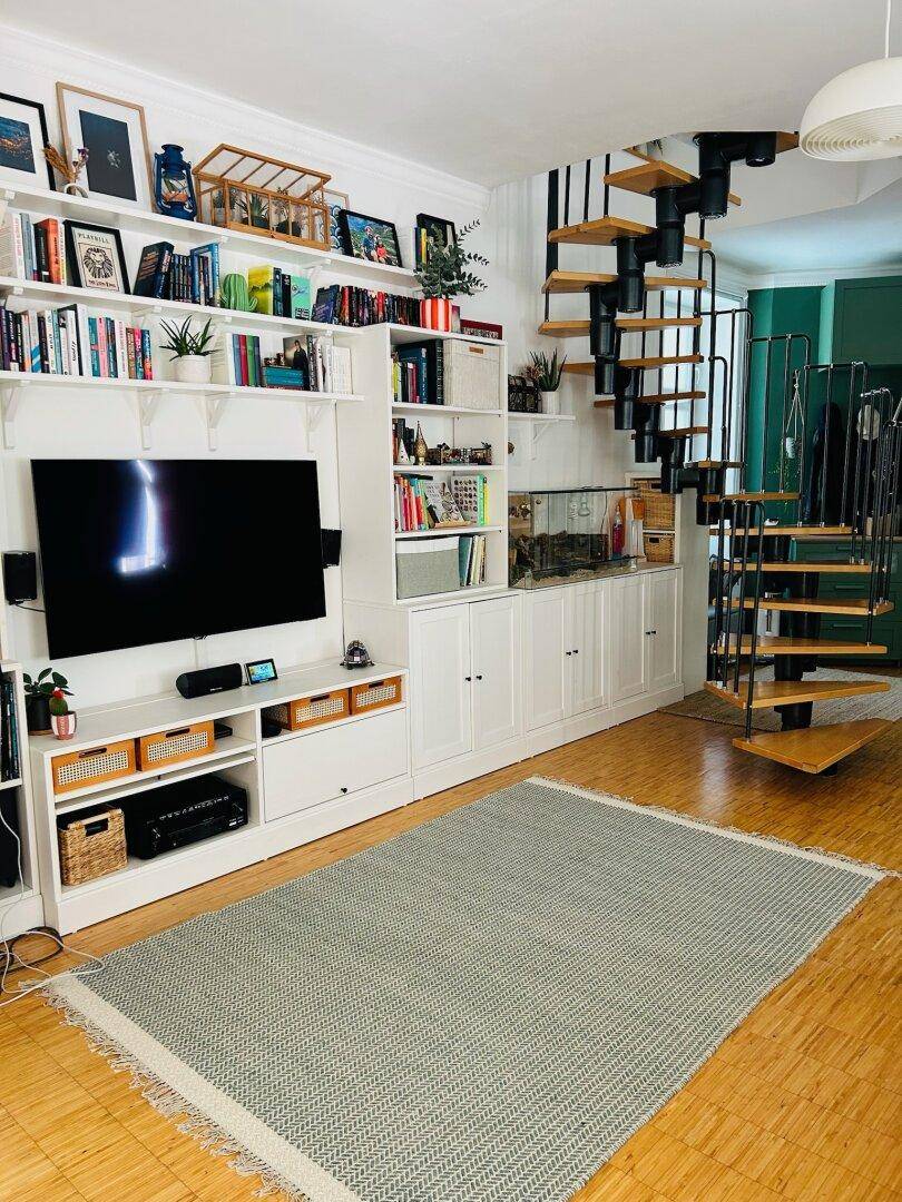Geräumiges Wohnzimmer mit großer Bücherwand, Fernseher und einer eleganten Wendeltreppe, die nach oben führt.