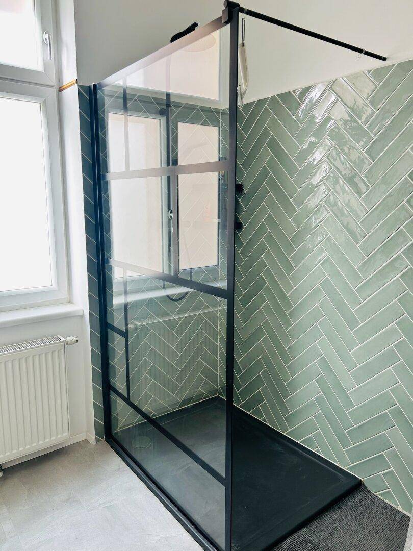 Moderne Duschkabine mit schwarzem Rahmen und mintgrünen Fischgrätfliesen, hell und stilvoll.